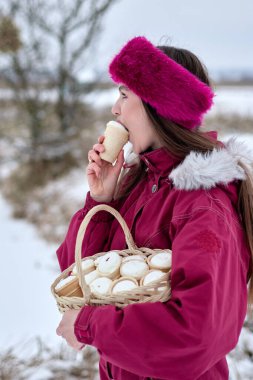 Büyüleyici genç bir kadın kışın dışarıda dondurma yiyor, pembe bir saç bandı takıyor ve kar altında bir sepet leziz koni taşıyor, mutlu ve mutlu görünüyor..