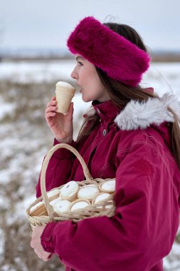 Kış sahnesinde, dondurmanın tadını çıkaran, kalın giyinmiş ve karlı bir zemine karşı aynı ikramlardan oluşan bir sepet taşıyan genç bir kadın manzaranın tadını çıkarıyor..