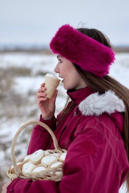 Mavi kürklü bir saç bandı takmış neşeli genç bir kadının dondurma külahının keyfini çıkarırken açık havada daha çok dondurma külahıyla dolu bir sepeti tutarken görüntüsü..