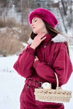 Pembe kürk şapkalı şık bir kadın, elinde bir sepet ile zarif bir şekilde poz veriyor, klasik moda ve dingin doğal güzelliğin bir karışımını sergiliyor..