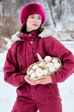 Sıcak bir kış elbisesi giymiş güzel bir genç kadın ve parlak pembe bir kürk şapkası karlı bir manzarada duruyor, dikkatle dondurma külahlarıyla dolu bir sepeti tutuyor, bakışları düşünceli bir şekilde yana bakıyor..