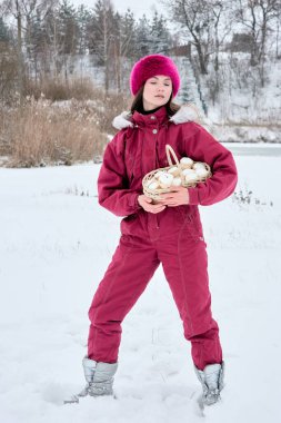 Karlı bir kış sahnesinde, macenta bir kar elbisesi giymiş bir kadın, doğada tuhaf ve mevsimsel bir an gösteren bir sepet dolusu marşmelovla poz verir..