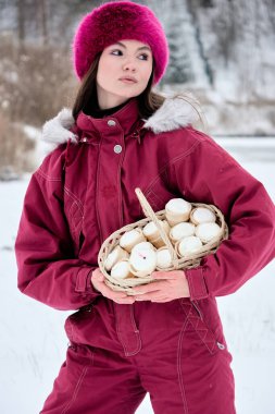 Büyüleyici bir sahnede zarif pembe bir şapka ve tulumla süslenmiş genç bir kadın zarif bir şekilde kar kaplı sakin bir kış manzarasının ortasında içi lezzetli dondurma külahlarıyla dolu bir sepeti tutuyor ve sıcaklığın enfes bir karşıtlığını resmediyor.