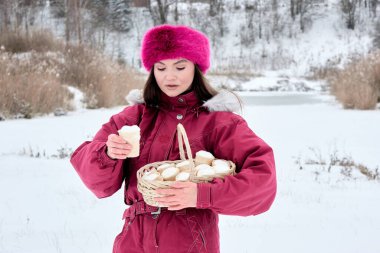 Kırmızı kayak takımı ve pembe kürk şapkalı çekici genç bir kadın. Karlı bir günün tadını çıkarıyor. Elinde dondurma külahlarıyla dolu bir sepet tutuyor ve kışın harikalar diyarının tadını çıkarıyor..