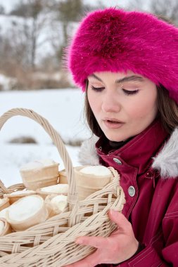 Canlı pembe kürk bir şapka ve şık bir kestane rengi kışlık ceket giymiş çekici genç bir kadın, kışın dışarıda dururken nefis dondurma külahlarıyla dolu enfes bir sepet tutuyor..