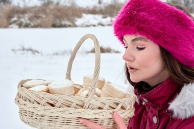 Tüylü pembe saç bandıyla parlak makyajlı çekici bir kadın kar yağışlı bir günde dondurma külahıyla dolu bir sepeti zarif bir şekilde tutuyor. Kış keyfi ve huzurlu bir gülümseme yaratıyor..