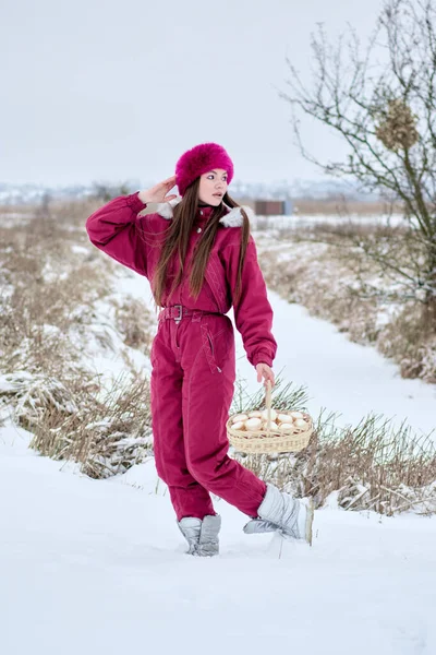 Canlı kırmızı bir kayak elbisesi, şık bir kürk şapkası ve zarif gümüş çizmeleri olan çekici genç bir kadın zarif bir sepetle güzel beyaz şekerlemelerle dolu bir sepet taşıyor karlı bir manzarada kışın cazibesinin özünü yakalıyor..