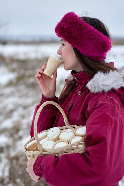 Pembe şapkalı ve rahat ceketli çekici genç bir kadın kış mevsiminde dondurma yemenin basit zevkinden zevk alıyor. Açık havada karlı bir ortamda içi dondurma dolu bir sepeti beşik gibi tutuyor..