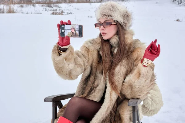 Kürk ceketli ve şapkalı zarif bir kadın kışın harikalar diyarında özçekim anını yakalıyor. Modayı teknolojiyle harmanlıyor. Eşsiz ve büyüleyici bir kış sahnesi sergiliyor..