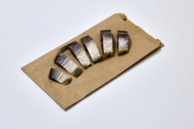 Stüdyo resmi, kahverengi bir kesekağıdının üzerinde soğuk tütsülenmiş ringa balığı dilimleri yakalıyor, el değmemiş beyaz bir yüzeye yerleştirilmiş, yemek blogları, aşçılık projeleri ve menü tasarım sunumları için ideal..