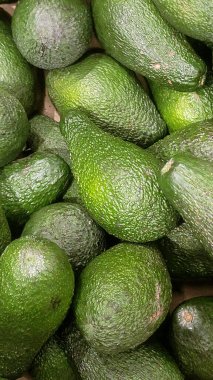 Bu çarpıcı yakın plan görüntüde taze yeşil avokadolar yığını var, dokulu yüzeylerini ve doğal ışıklarını yakalıyorlar, sağlık, gıda veya canlı arkaplan görüntüleri için mükemmel..