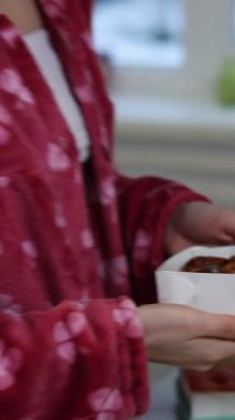 Hoş bir pijama seti içindeki neşeli genç kadın elinde lezzetli pastalarla dolu bir kutu, yüzünde mutlulukla ışıldayan yüzü parlak bir mutfakta bunu bekliyor..