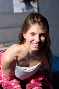 Büyüleyici bir görüntü, dairesinde gülümserken mutluluk ve neşe saçan genç bir kadını yansıtıyor, rahat kırmızı bir bornoz giyiyor, rahat ve davetkar bir atmosfer yaratıyor, dışarıdaki bulutlu gün ortama sükunet katıyor.,