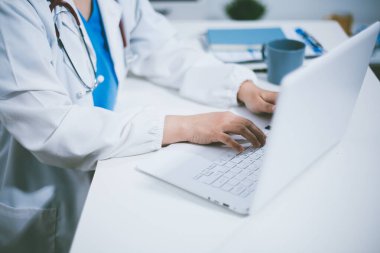 Doktorun odasında dizüstü bilgisayarla çalışan orta yaşlı bir kadın doktor.