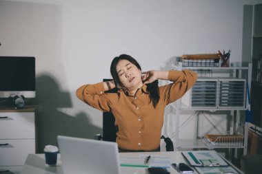 Asyalı kadın muhasebeci, ofiste çalışırken rahatlamak ve dinlenmek için sandalyede çalışmaktan yoruldu.