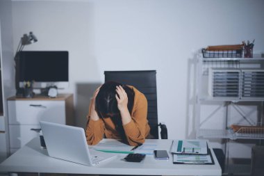 Bir kadın muhasebeci, ofis masasında dizüstü bilgisayarı üzerinde çalışırken bile başı ağrıyacak kadar belgelerle çalışmaktan stres altındaydı..