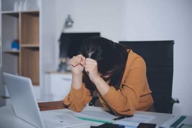 Bir kadın muhasebeci, ofis masasında dizüstü bilgisayarı üzerinde çalışırken bile başı ağrıyacak kadar belgelerle çalışmaktan stres altındaydı..