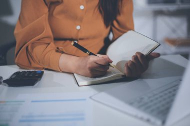 Business woman using calculator to calculate financial report, working at office with laptop computer on table. Asian female accountant or banker making calculations. finances and economy concept
