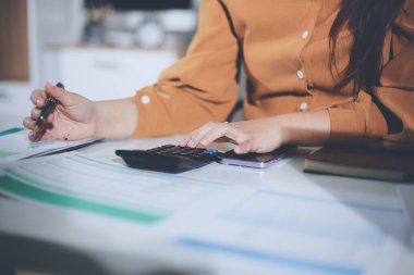 Business woman using calculator to calculate financial report, working at office with laptop computer on table. Asian female accountant or banker making calculations. finances and economy concept