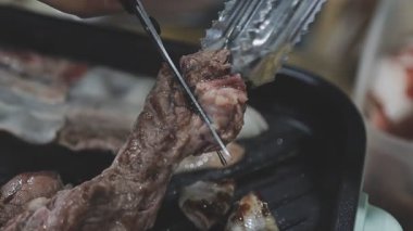 Galbi cızırdayan Kore barbekü deneyimi otantik restoran sahnesi için duman ve ızgara izleriyle dinamik pişirme hareketleri gösteriyor.