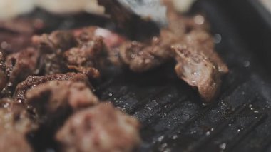 Galbi cızırdayan Kore barbekü deneyimi otantik restoran sahnesi için duman ve ızgara izleriyle dinamik pişirme hareketleri gösteriyor.