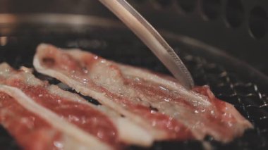 Galbi cızırdayan Kore barbekü deneyimi otantik restoran sahnesi için duman ve ızgara izleriyle dinamik pişirme hareketleri gösteriyor.