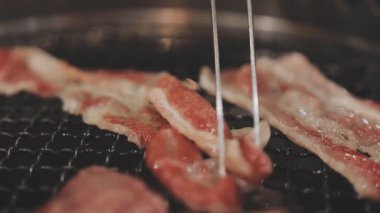 Galbi cızırdayan Kore barbekü deneyimi otantik restoran sahnesi için duman ve ızgara izleriyle dinamik pişirme hareketleri gösteriyor.