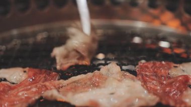 Galbi cızırdayan Kore barbekü deneyimi otantik restoran sahnesi için duman ve ızgara izleriyle dinamik pişirme hareketleri gösteriyor.