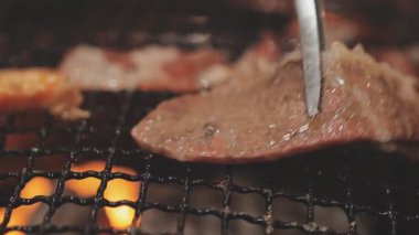 Galbi cızırdayan Kore barbekü deneyimi otantik restoran sahnesi için duman ve ızgara izleriyle dinamik pişirme hareketleri gösteriyor.