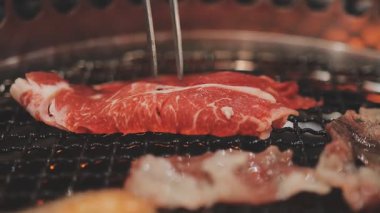 Galbi cızırdayan Kore barbekü deneyimi otantik restoran sahnesi için duman ve ızgara izleriyle dinamik pişirme hareketleri gösteriyor.