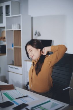 Asyalı kadın muhasebeci, ofiste çalışırken rahatlamak ve dinlenmek için sandalyede çalışmaktan yoruldu.