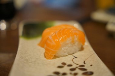 A piece of salmon sushi rests elegantly on a decorative plate in a restaurant. The sushi features vibrant orange fish on top of sticky rice, highlighting a traditional culinary art.