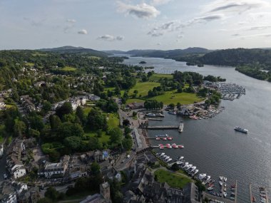 Aerial view of Windermere Lake showcasing green hills, charming homes, and a bustling marina filled with boats, capturing the beauty of summer in the Lake District.