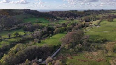 A beautiful aerial view captures green hills and valleys in the countryside. Sunlight highlights the trees and fields, creating a peaceful and serene atmosphere.