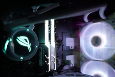 Canlı RGB ışıkları gece karanlık bir odada parlak bir bilgisayar sistemini aydınlatıyor. Parçaları arasında şık bir RAM ve soğutma vantilatörleri var. Teknoloji meraklısı bir ortam sergiliyorlar..
