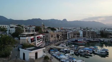 Kuzey Kıbrıs 'taki bir limanda çarpıcı bir günbatımı. Tekneler suda düzgünce düzenlenirken binalar görkemli dağlara karşı kıyıya dizilir..