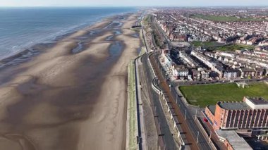 Sahil manzarası, kıyı boyunca uzanan sakin dalgalarla dolu kumlu bir sahile sahipken, canlı bir sahil kasabası gün ışığında açık gökyüzünün altında uzanıyordu..