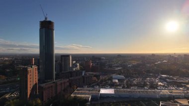 Parlak günbatımı, modern binaların ve devam eden inşaatların karışımının yer aldığı bir şehir silueti üzerinde sıcak bir parıltı yayıyor. Sahne kentsel yaşamın ve gelişimin özünü yakalıyor..