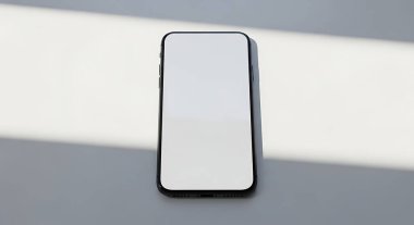 Pürüzsüz, beyaz ekranlı modern bir akıllı telefon, doğal güneş ışığıyla vurgulanmış, temiz, minimalist gri ve beyaz bir arka plana yerleştirilir ve farklı gölgeler yaratır..