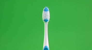 Mavi aksanlı bir diş fırçasının, canlı yeşil bir arka plana karşı yakın plan çekimi, diş hijyeni ve oral bakım uygulamalarını vurguluyor.