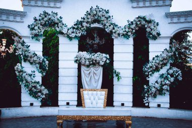 Beyaz bir arkaplanda zarif bir çiçek aranjmanı, muhtemelen düğün ya da etkinlik için. Bir sandalye ve örtülü kumaş..