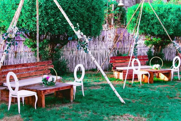 Açık hava oturma düzenleme ahşap banklar ve masalar, beyaz sandalyeler ve bir bahçe düzenleme çiçek dekorasyonları.
