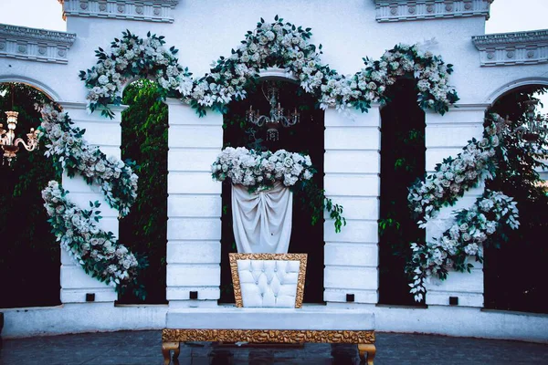 Beyaz bir arkaplanda zarif bir çiçek aranjmanı, muhtemelen düğün ya da etkinlik için. Bir sandalye ve örtülü kumaş..