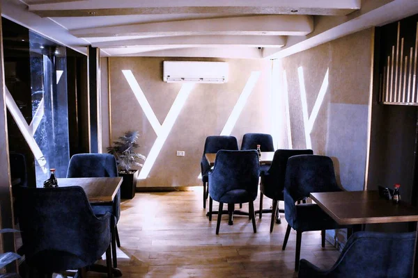 Koyu mavi sandalyeli, ahşap masalı ve dekoratif ışıklandırmalı modern bir restoran..