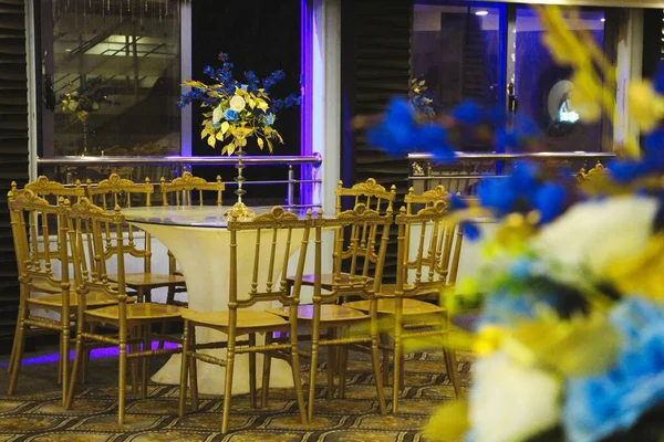 Beyaz masa örtüsü, altın koltuklar ve mavi ve sarı çiçekli bir masa. Kutlama etkinliği için..