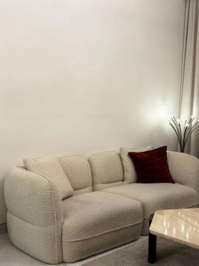 Tarafsız renkli oturma odası, pofuduk beyaz bir kanepe, kırmızı aksanlı yastık, mermer masa ve şık bir lamba..