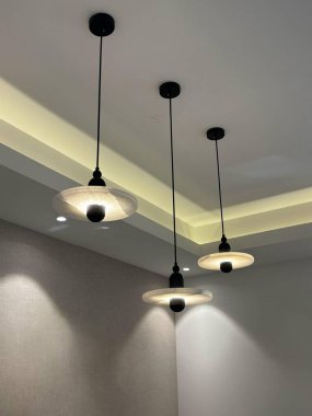 Beyaz bir tavandan sarkan üç modern kolye ışığı, sıcak bir ışık saçıyor..