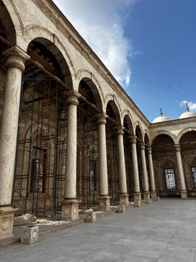 Mavi gökyüzünün altında sütunları ve kemerleri olan bir binanın mimari görüntüsü. Tadilat yapılan tarihi bir yer gibi görünüyor..