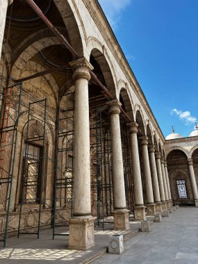 Muhammed Ali Camii 'nin avlusunda beyaz sütunlar tarafından desteklenen kemerler, mavi gökyüzü ile çevrili..