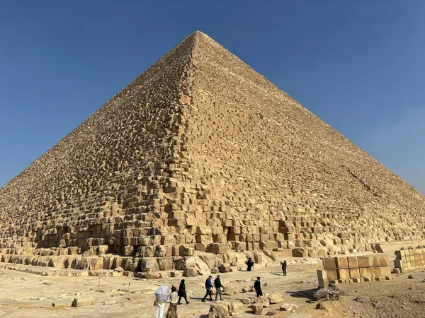 Kahire, Mısır - 01: 15 2025: Büyük Giza Piramidi açık mavi bir gökyüzünün altında çevresindeki çöl manzarasını keşfeden turistlerle birlikte duruyor..